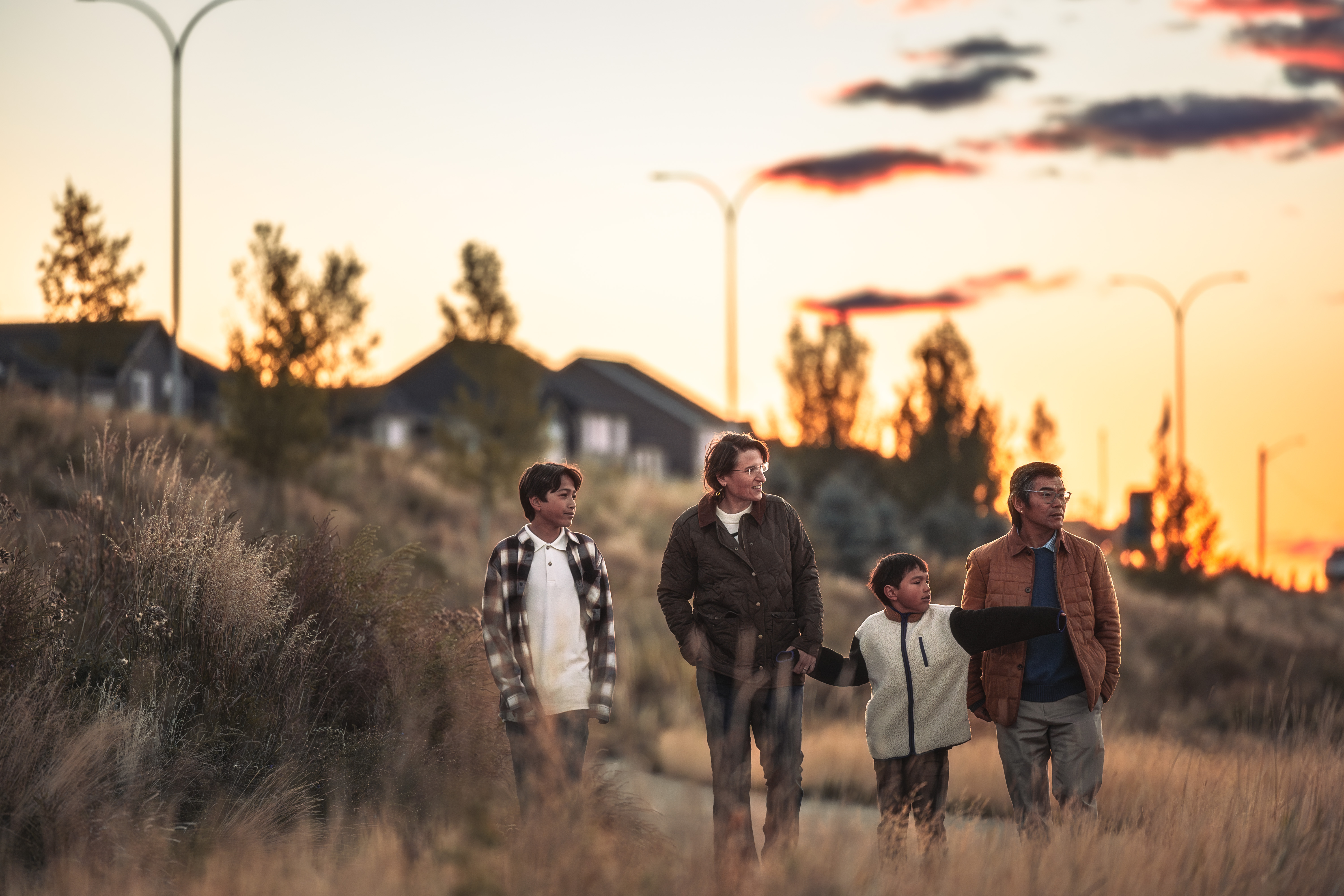 Family walks on pathway along tall grass in community at dusk